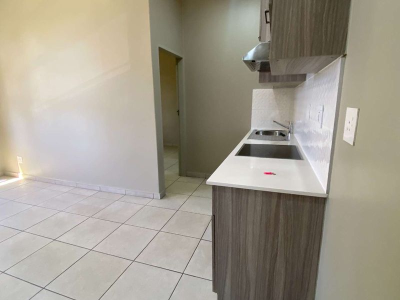 A compact, modern kitchen featuring wood-finish cabinetry, a stainless steel sink, an extractor fan, and neutral tiled flooring.