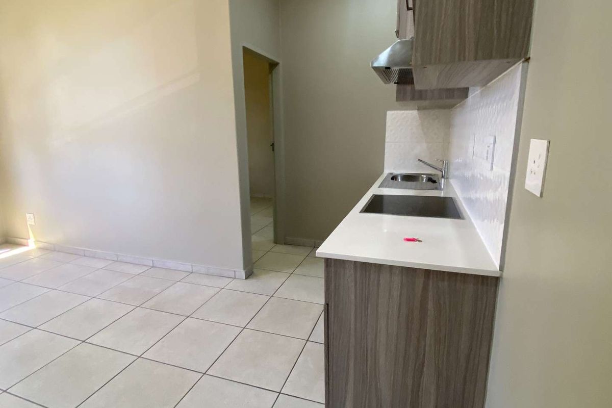A compact, modern kitchen featuring wood-finish cabinetry, a stainless steel sink, an extractor fan, and neutral tiled flooring.