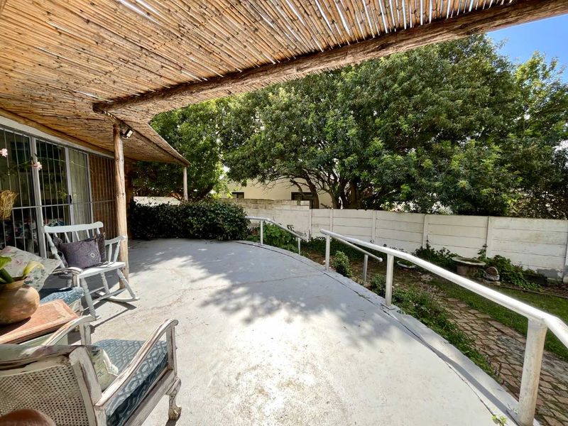 Covered outdoor patio area featuring a bamboo roof structure, concrete flooring, and metal safety railings overlooking a private garden space.