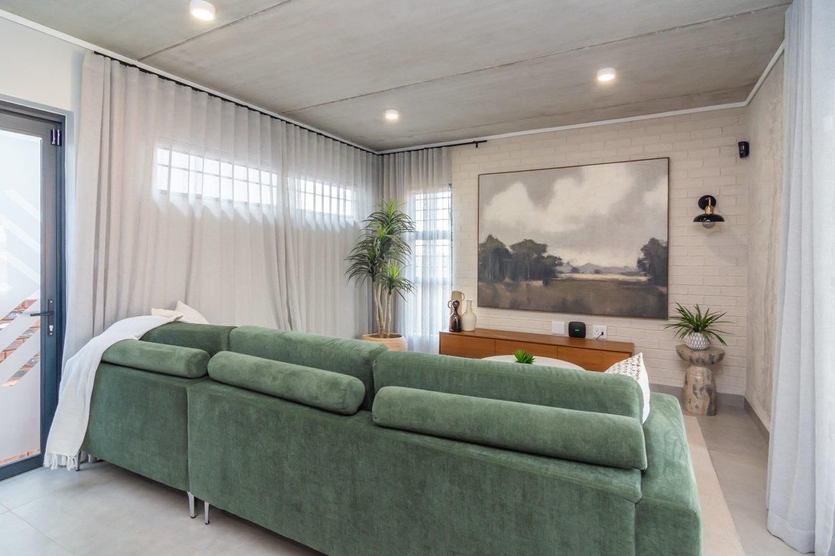 Modern living room featuring an exposed concrete ceiling, painted brick feature wall, tiled flooring, and recessed lighting with access to an outdoor area.