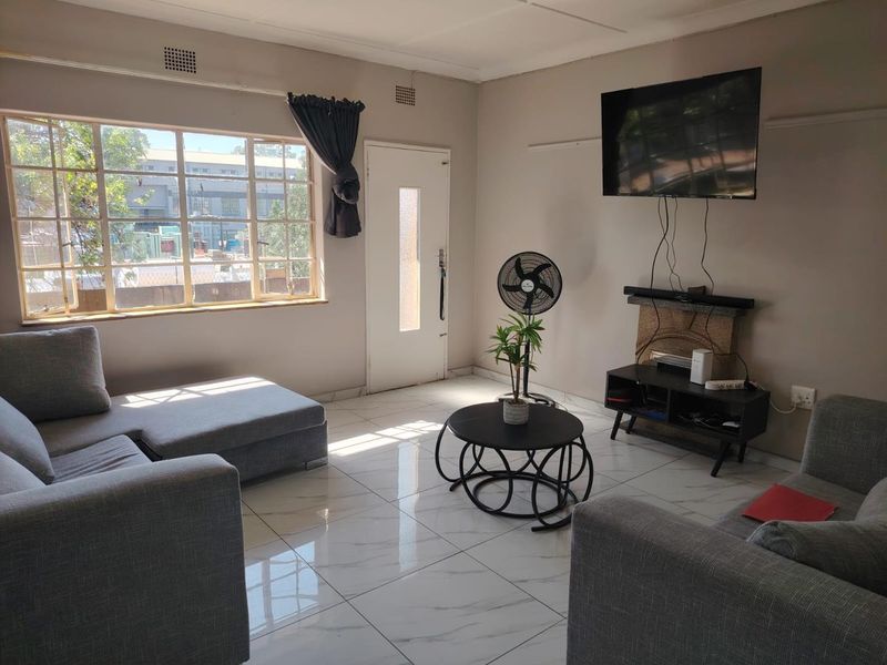 A bright living room featuring large windows, modern white marble-look floor tiles, and a neutral wall finish, providing a clean and functional living space.