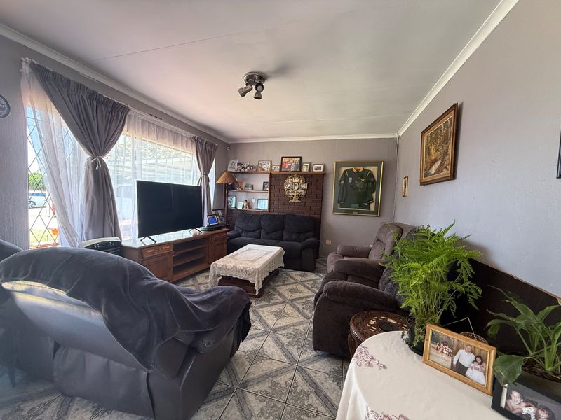 A living room featuring tiled flooring, a brick fireplace with built-in shelving, and large windows allowing natural light.