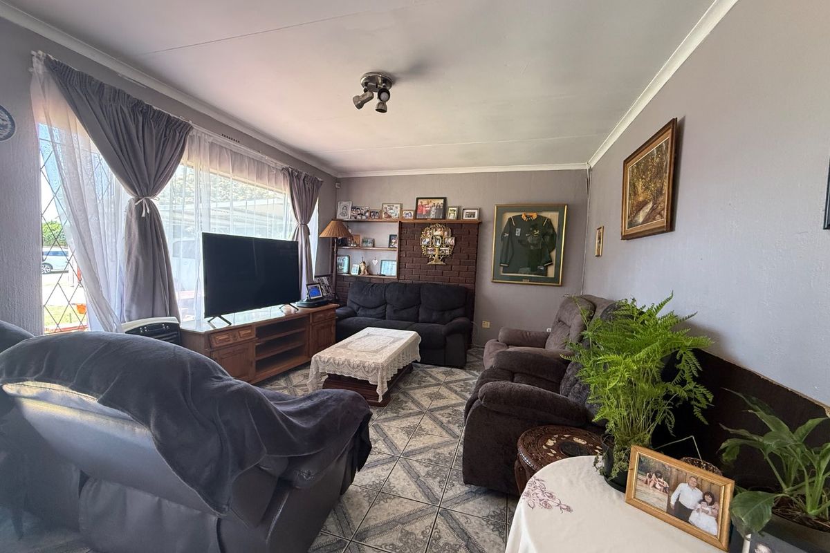 A living room featuring tiled flooring, a brick fireplace with built-in shelving, and large windows allowing natural light.