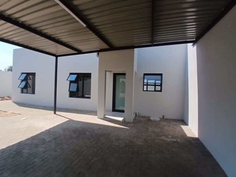 A modern townhouse exterior featuring a covered carport, paved driveway, and clean white facade with contemporary aluminium-framed windows and a glass entrance door.