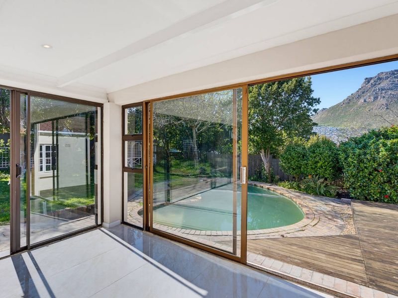 Covered patio area featuring large sliding glass doors, tiled flooring, and direct access to a swimming pool and timber deck with mountain views.