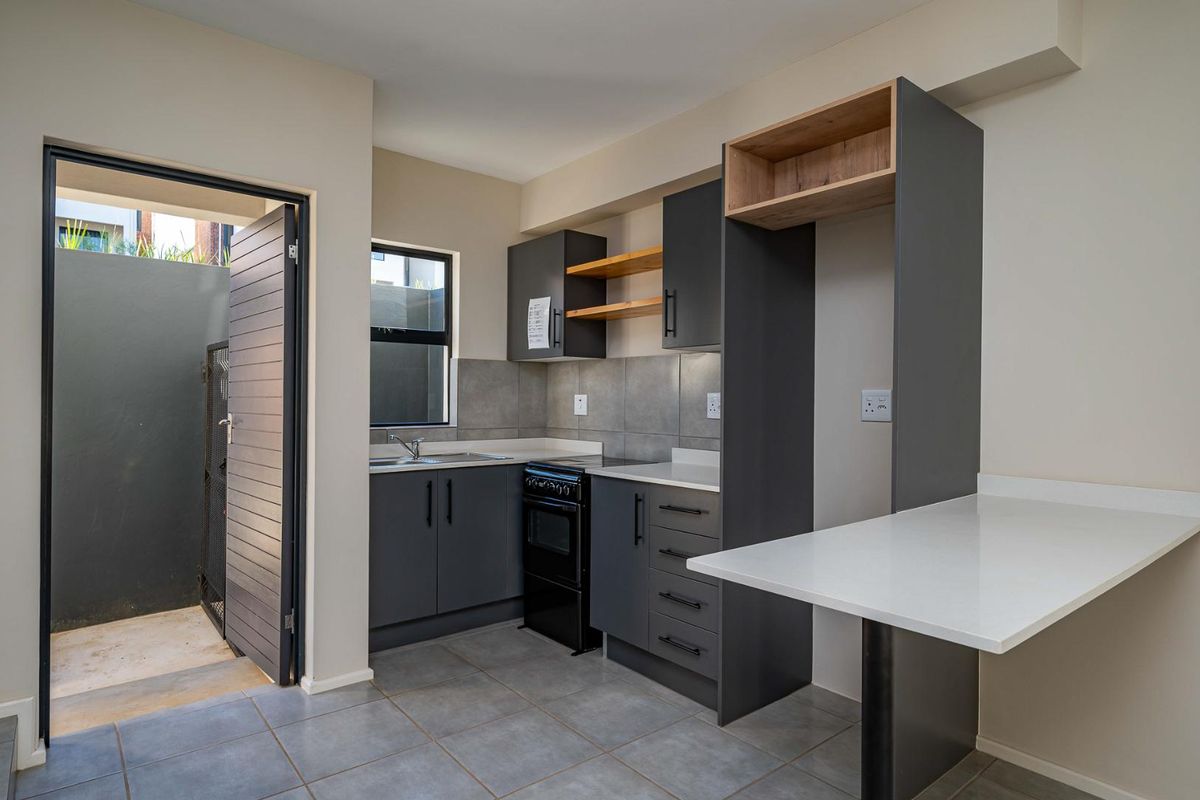 Modern kitchen featuring dark grey cabinetry, stone countertops, a built-in oven, and direct access to an enclosed outdoor utility area.