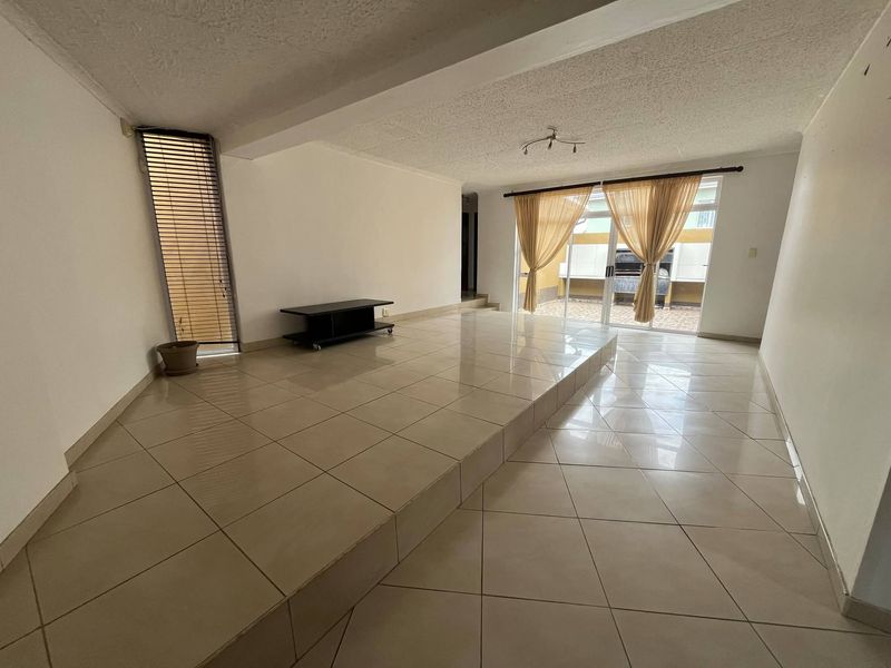 Spacious living area featuring a unique raised tiled platform, textured ceiling, and sliding glass doors providing access to the outdoor patio area.