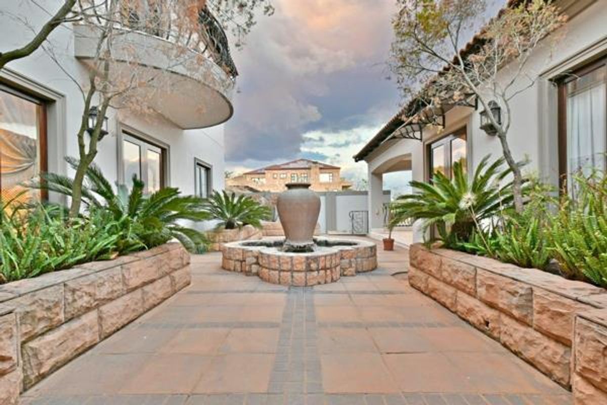 A beautifully landscaped courtyard featuring a central stone fountain, paved walkways, and raised stone planters between two wings of the residence.