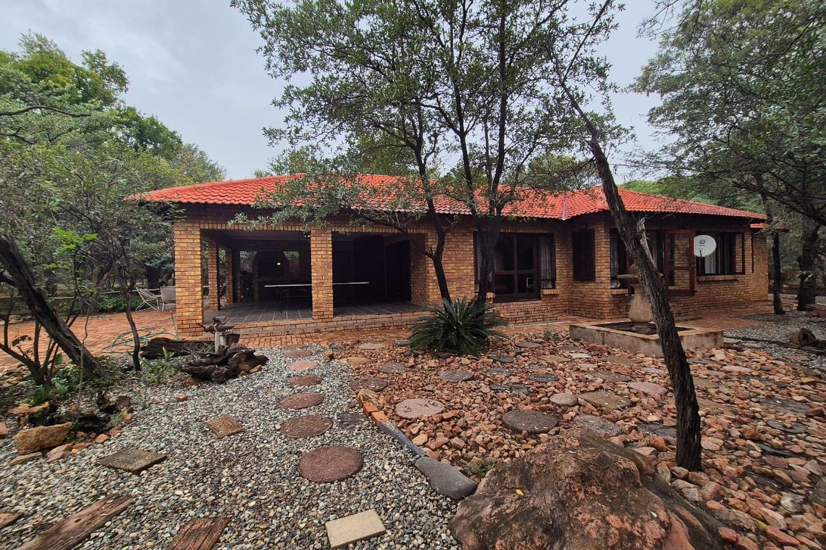 A rustic face-brick house featuring a covered patio area, tiled roof, and a landscaped garden with stone pathways and a water feature.