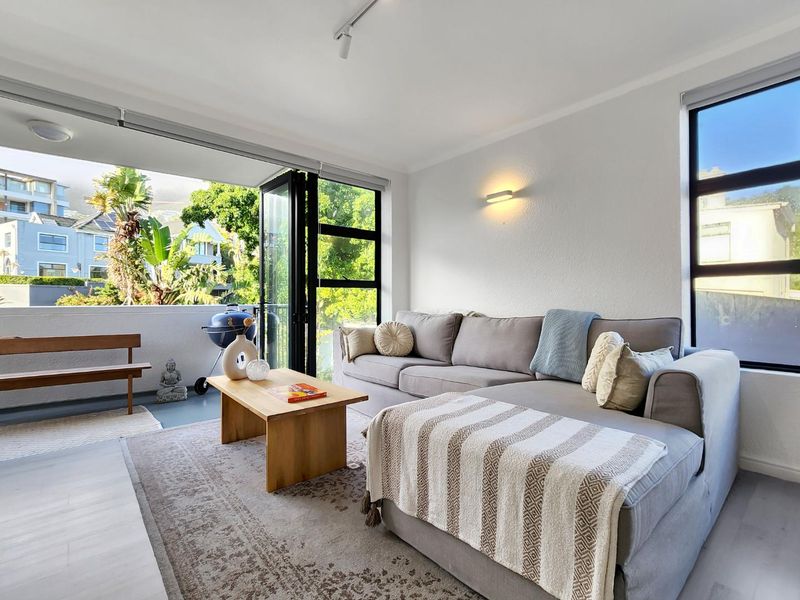 Bright open-plan living area featuring large windows and bi-fold doors that open onto a private balcony, creating a seamless indoor-outdoor flow.