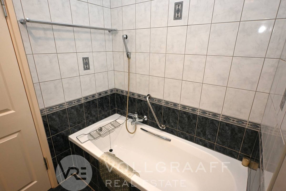 A functional bathroom featuring a bathtub with a handheld shower attachment, grab rail, and decorative ceramic wall tiling.