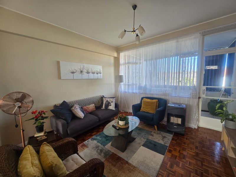 A cozy living room featuring classic parquet flooring, large windows allowing natural light, and access to an adjoining balcony area.