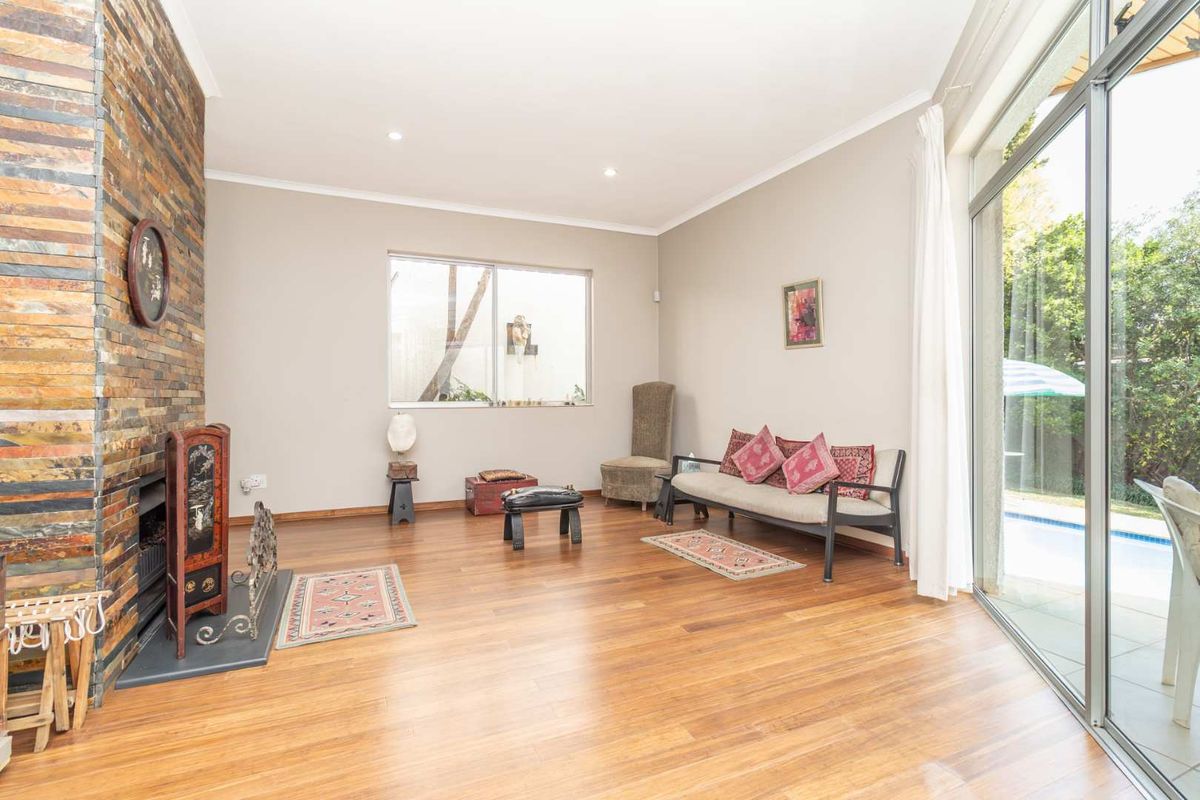 Spacious living room featuring hardwood flooring, a striking stone-clad fireplace, and large sliding glass doors providing seamless access to the outdoor pool area.
