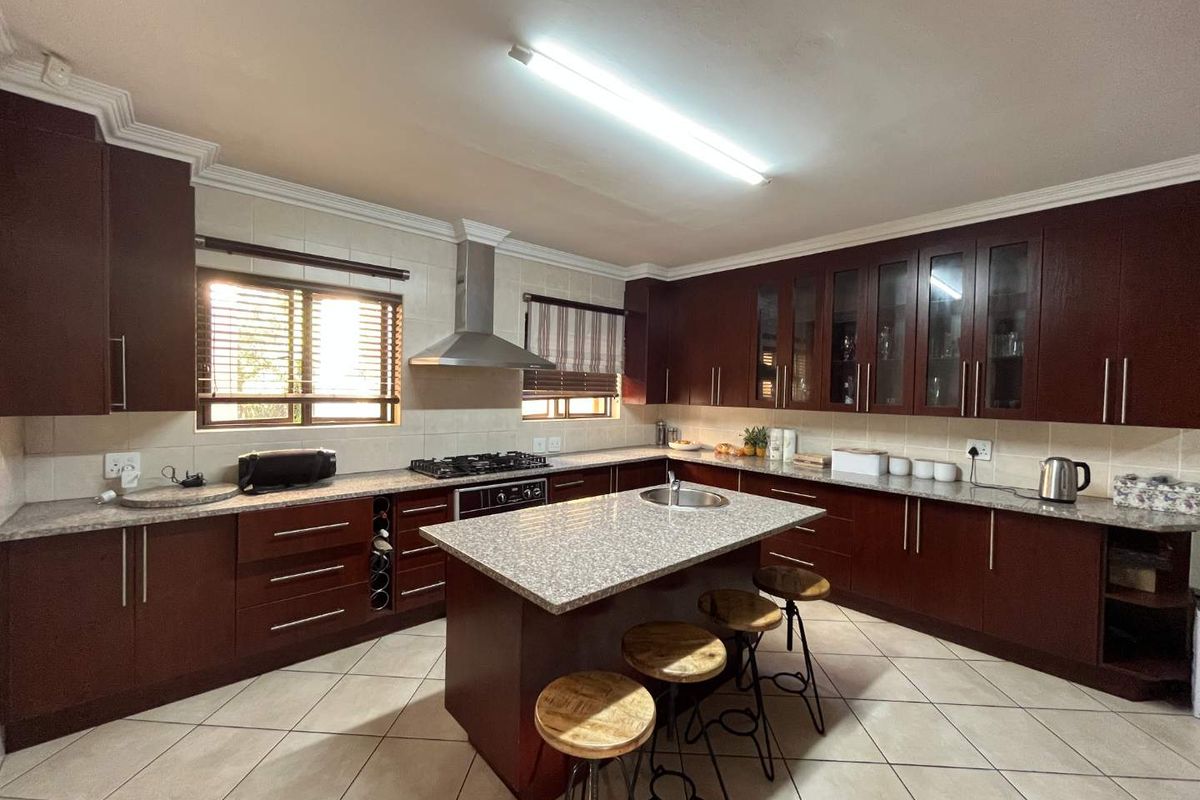 Spacious kitchen featuring dark wood cabinetry, granite countertops, a central island with a prep sink, and a stainless steel extractor fan.