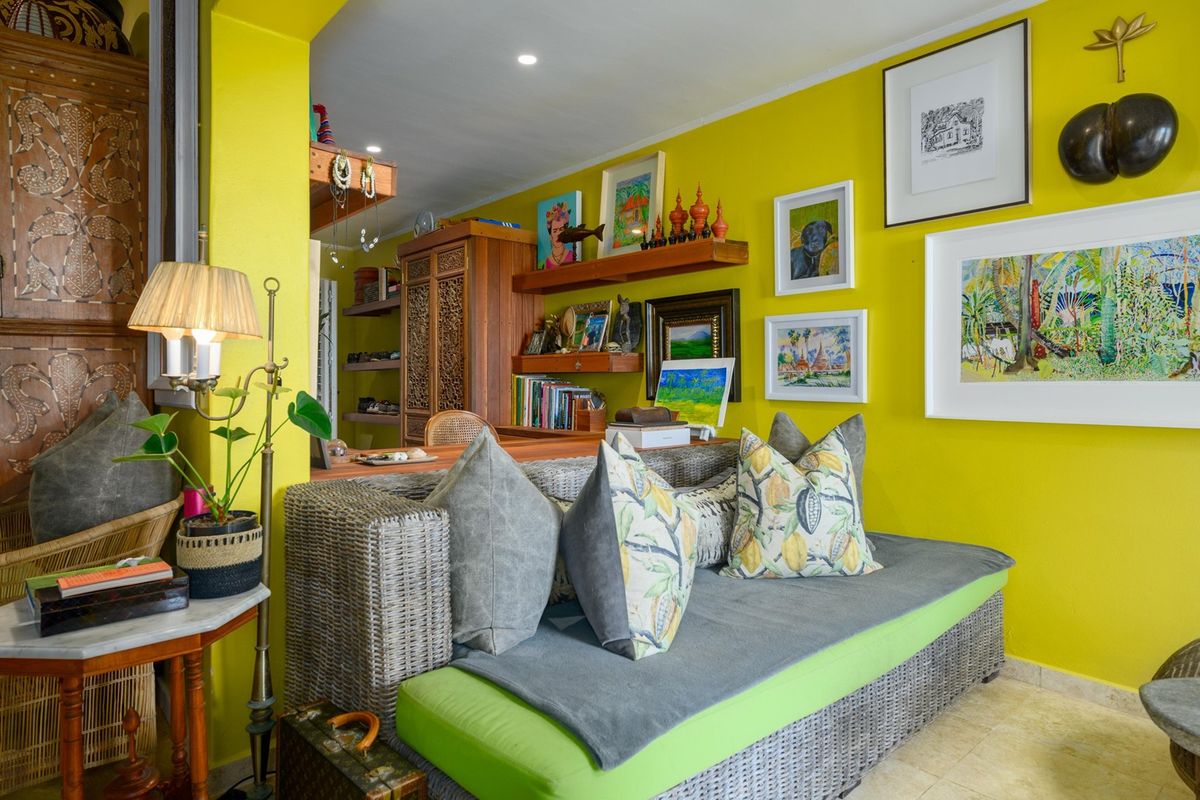 A vibrant living room featuring bright yellow walls, stone tile flooring, and built-in wooden shelving, creating a warm and eclectic atmosphere.