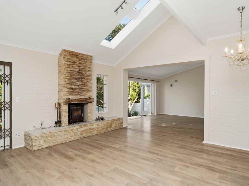 Spacious living area featuring a vaulted ceiling with skylights, stone fireplace with wood-burning stove, and modern laminate flooring.