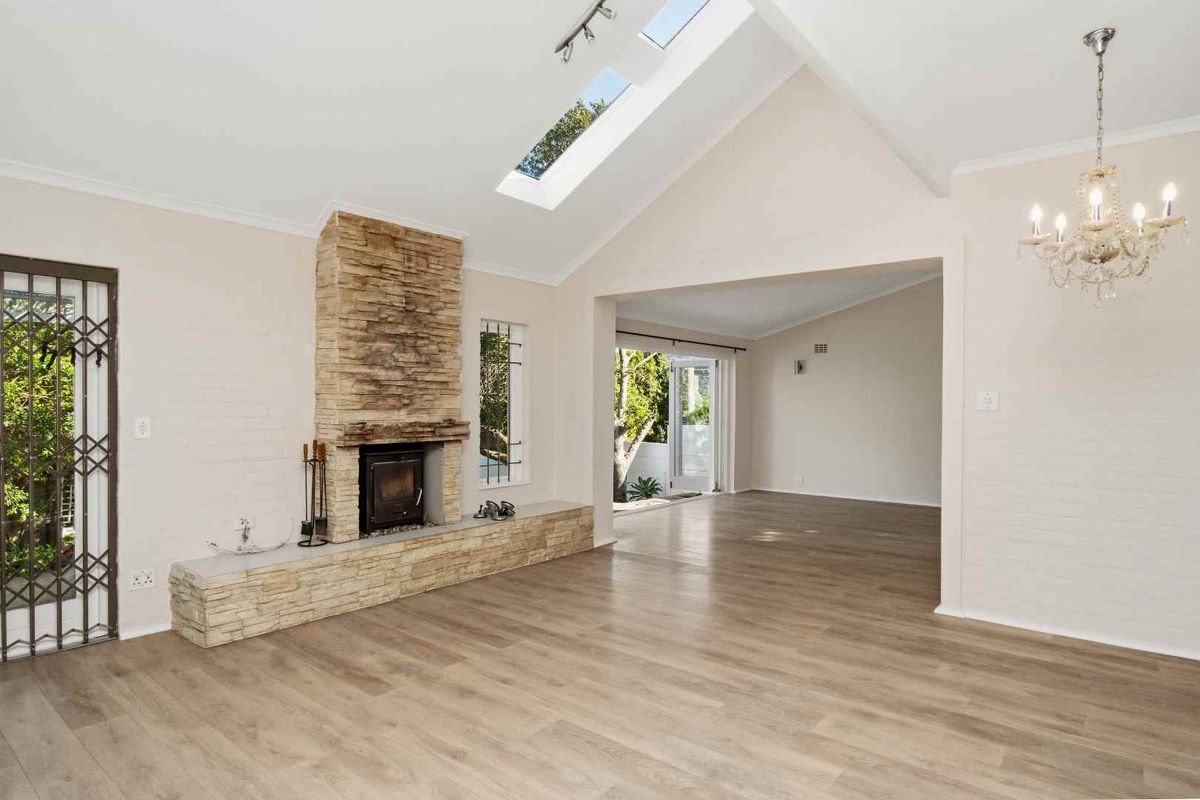Spacious living area featuring a vaulted ceiling with skylights, stone fireplace with wood-burning stove, and modern laminate flooring.