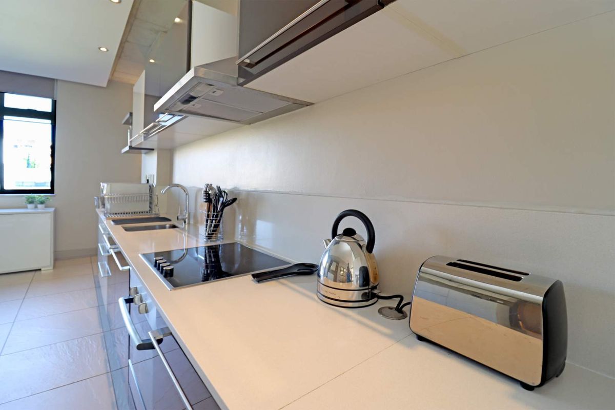 Modern kitchen featuring sleek cabinetry, integrated hob, extractor fan, and stone countertops in a clean, contemporary apartment setting.