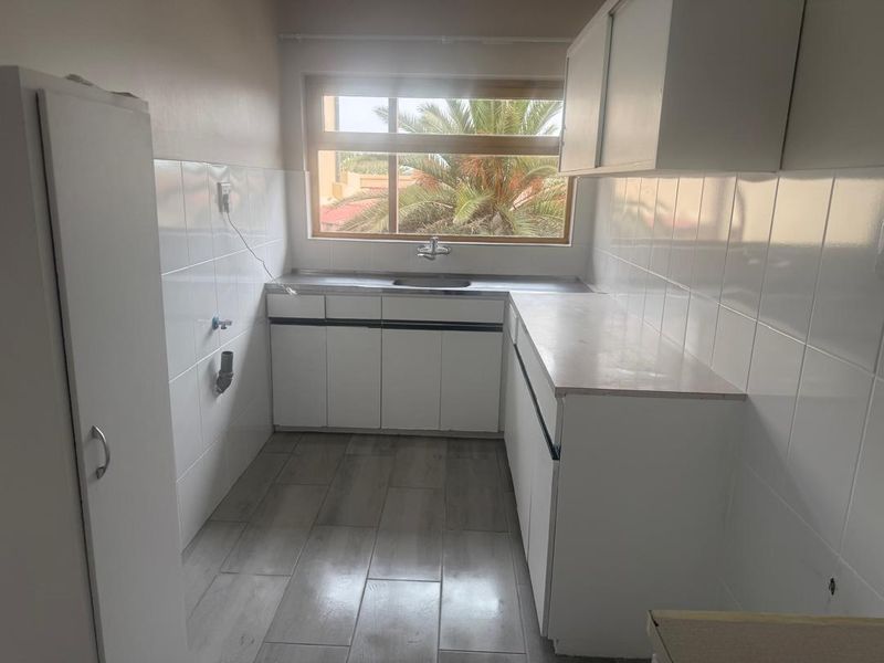 A functional scullery or laundry area featuring built-in white cabinetry, a stainless steel sink, tiled splashbacks, and modern grey floor tiles.