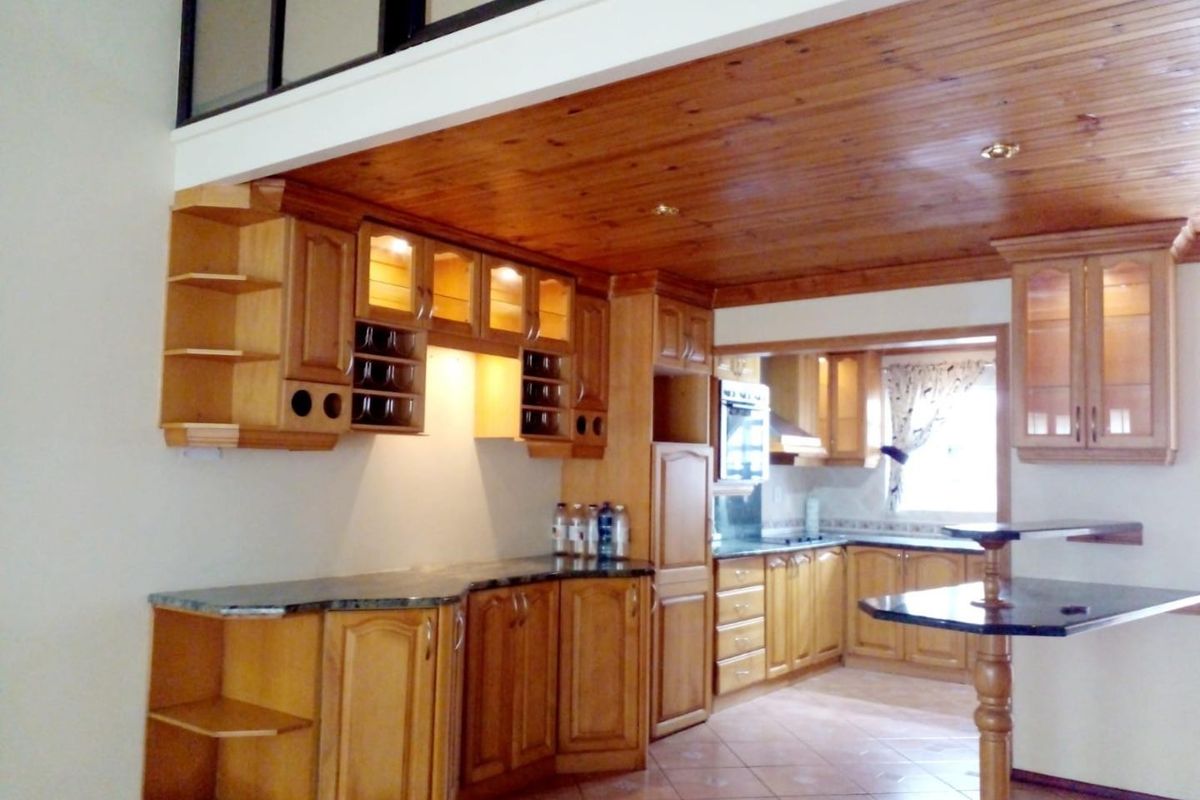 Spacious kitchen featuring extensive wooden cabinetry, granite countertops, a built-in oven, and a distinctive timber ceiling, offering a functional layout with a breakfast bar.