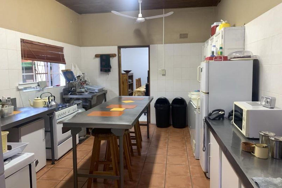 A functional kitchen featuring stainless steel countertops, tiled flooring, and wall splashbacks, with a timber ceiling and integrated gas stove.