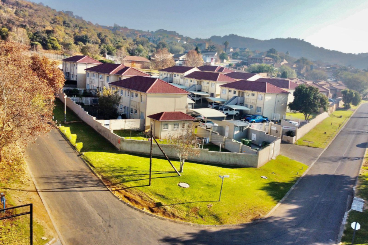 Aerial view of an apartment complex featuring multiple residential buildings with tiled roofs, paved driveways, and perimeter walling in a suburban setting.