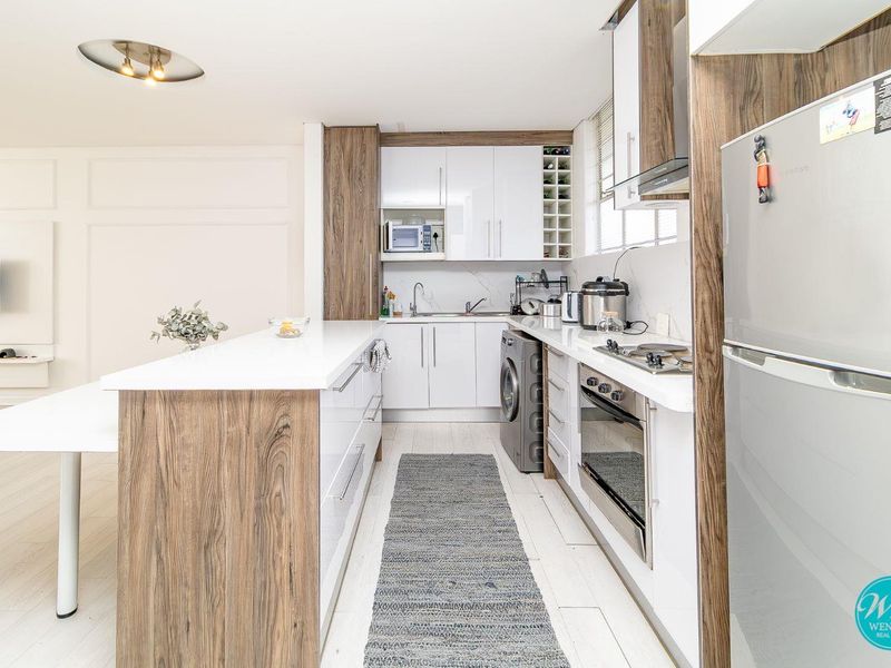 Modern kitchen featuring white high-gloss cabinetry, wood-grain accents, stone countertops, integrated appliances, and a functional breakfast island.