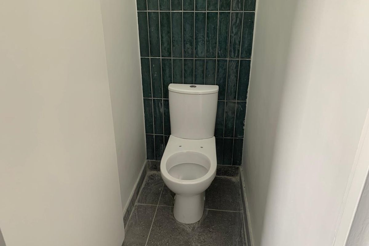 A compact bathroom featuring a modern white toilet, dark grey floor tiling, and a decorative teal tiled feature wall.