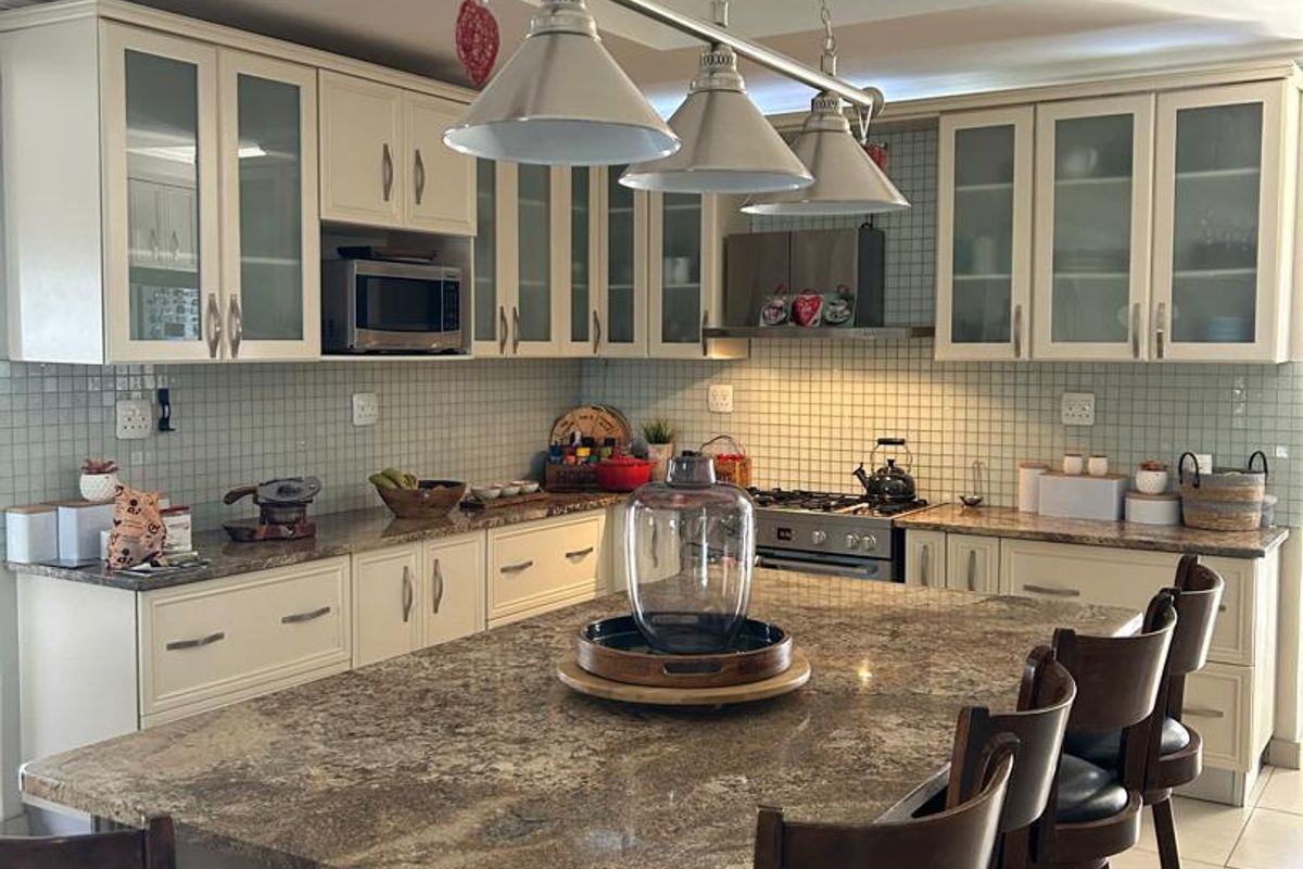 A well-appointed kitchen featuring granite countertops, a central island with breakfast bar seating, glass-front cabinetry, and a built-in gas hob with extractor fan.