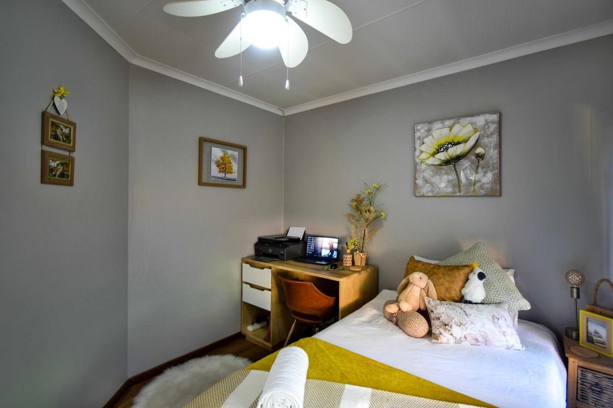 A cozy bedroom featuring neutral grey walls, a ceiling fan, and wood-look flooring, providing a comfortable and functional living space.