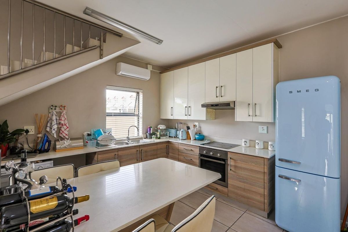 Modern kitchen featuring wood-grain and cream cabinetry, stone countertops, built-in oven, extractor fan, and a split-system air conditioning unit.