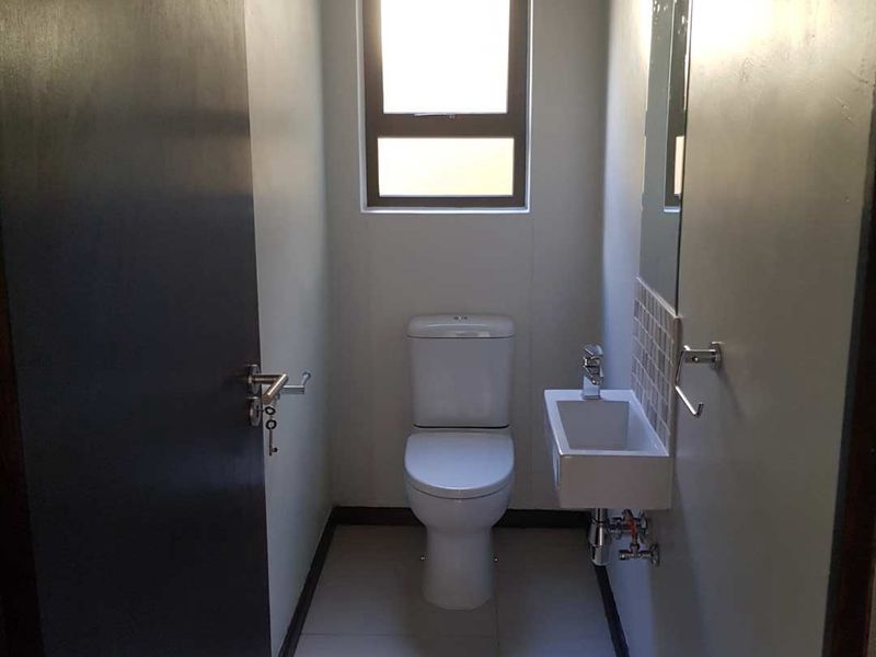 A compact guest bathroom featuring a modern wall-mounted basin, toilet, and neutral floor tiling.