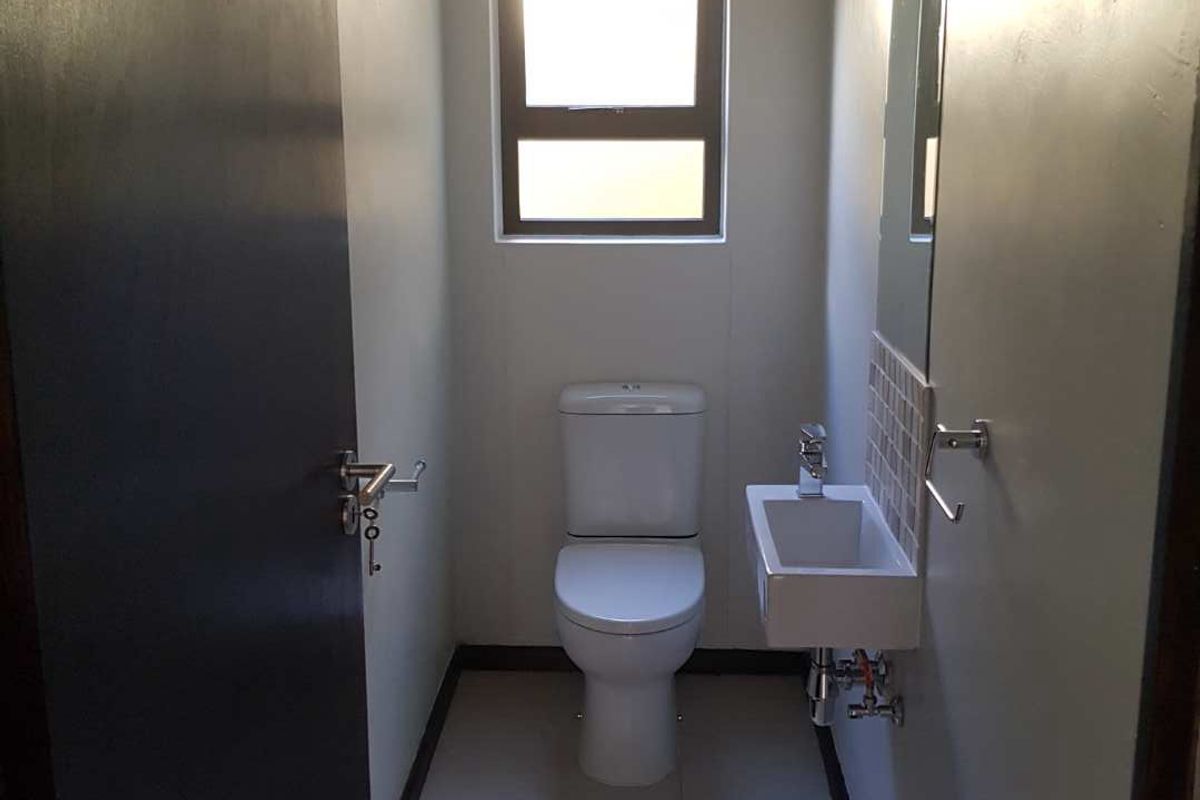 A compact guest bathroom featuring a modern wall-mounted basin, toilet, and neutral floor tiling.