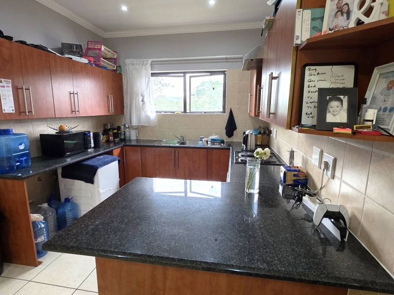 A functional kitchen featuring granite countertops, ample wooden cabinetry, a stainless steel sink, and a tiled backsplash with integrated extractor fan.