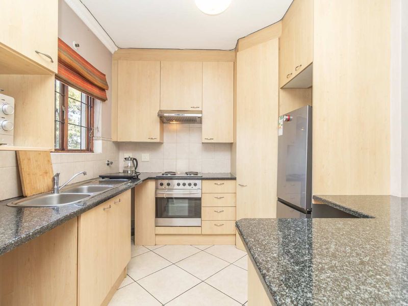A functional kitchen featuring light wood laminate cabinetry, granite countertops, a built-in oven with hob, and tiled flooring.