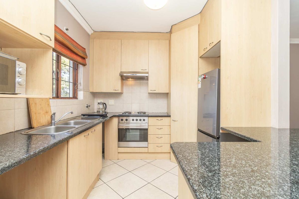 A functional kitchen featuring light wood laminate cabinetry, granite countertops, a built-in oven with hob, and tiled flooring.