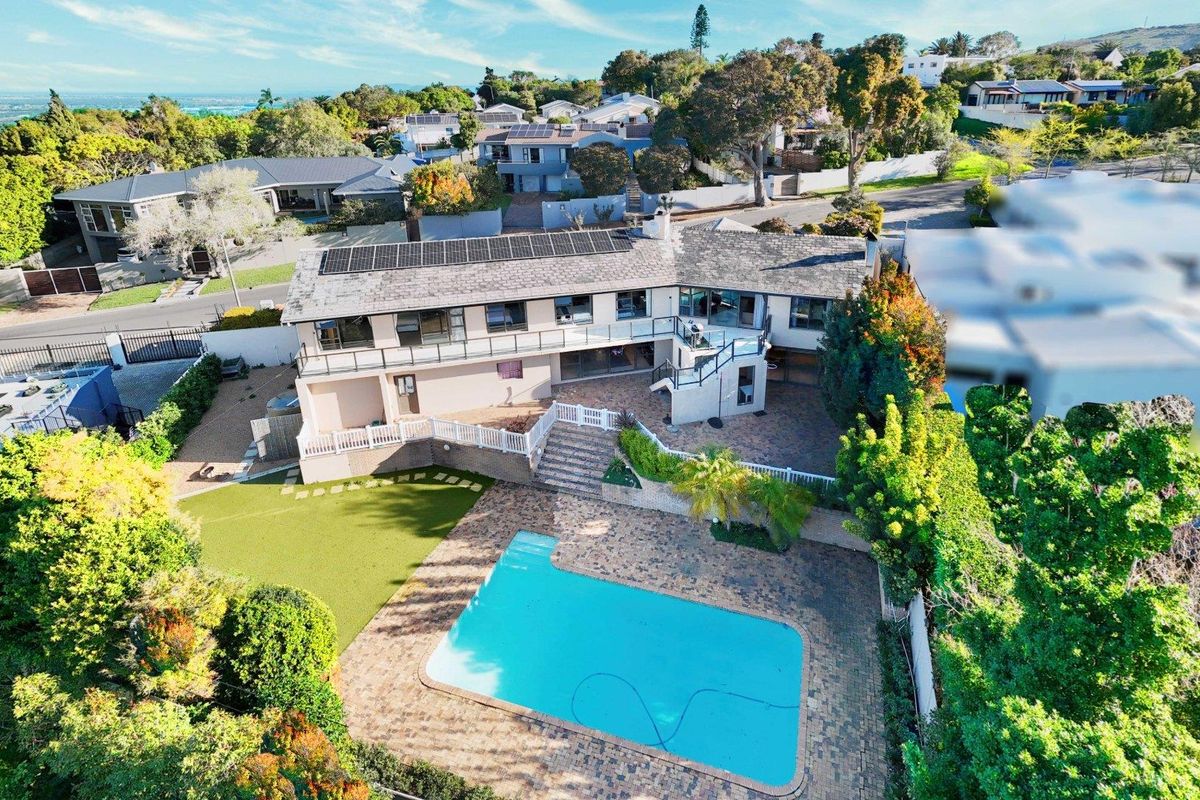 Aerial view of a residential property featuring a swimming pool, paved patio area, balcony, and solar panels on the roof.