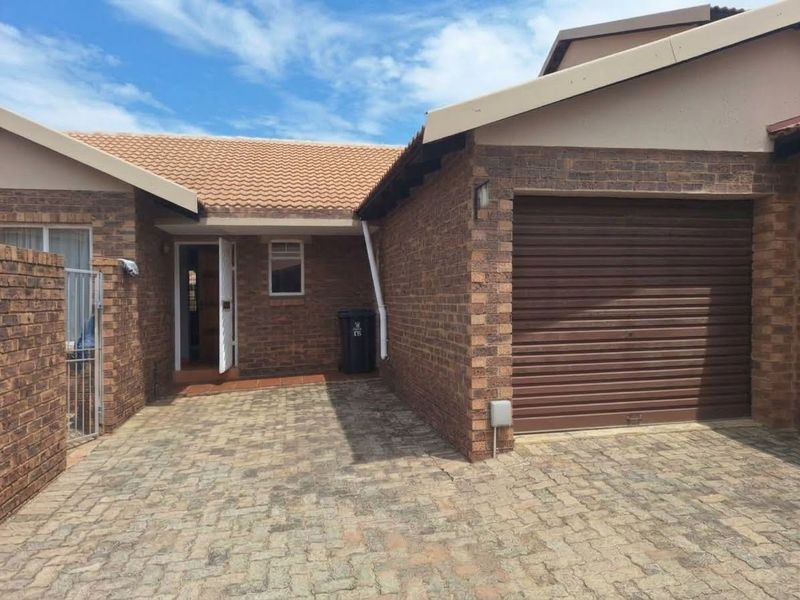Front exterior view of the townhouse featuring a brick facade, tiled roof, paved driveway, and a secure roller garage door.