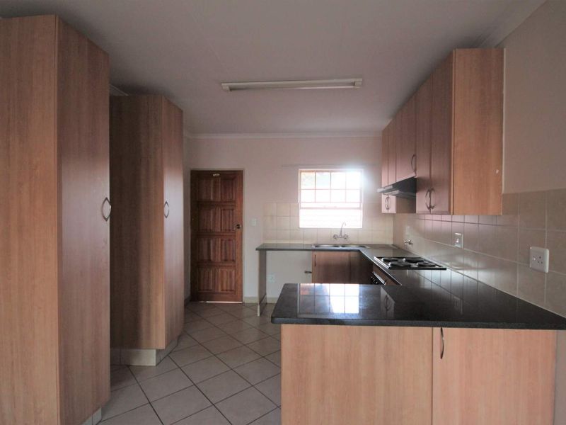A functional kitchen featuring light wood-finish cabinetry, dark laminate countertops, a built-in hob with extractor fan, and tiled flooring.