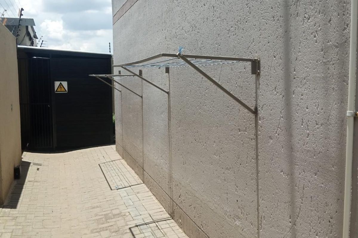A paved side exterior area featuring wall-mounted folding drying racks and a secure gated entrance.