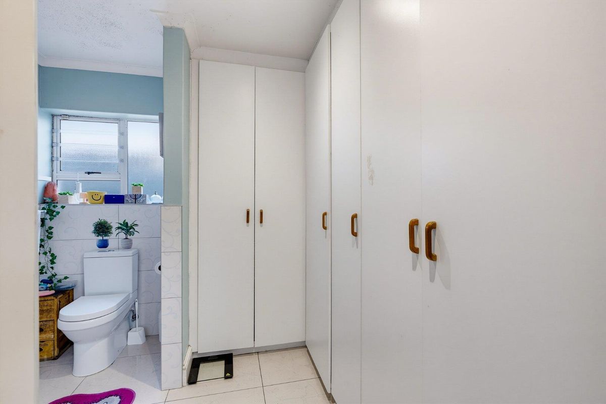 Bathroom featuring built-in storage cupboards, tiled flooring, and a toilet positioned near an obscured glass window.