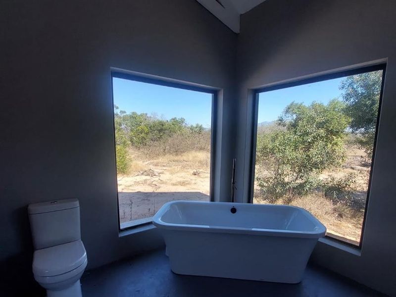 Modern bathroom featuring a freestanding bathtub, toilet, and expansive corner windows offering scenic natural views with a vaulted ceiling.