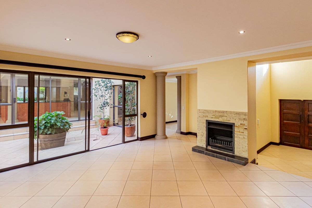 Spacious living area featuring tiled flooring, a built-in fireplace with stone cladding, decorative columns, and large sliding glass doors opening to an internal courtyard.