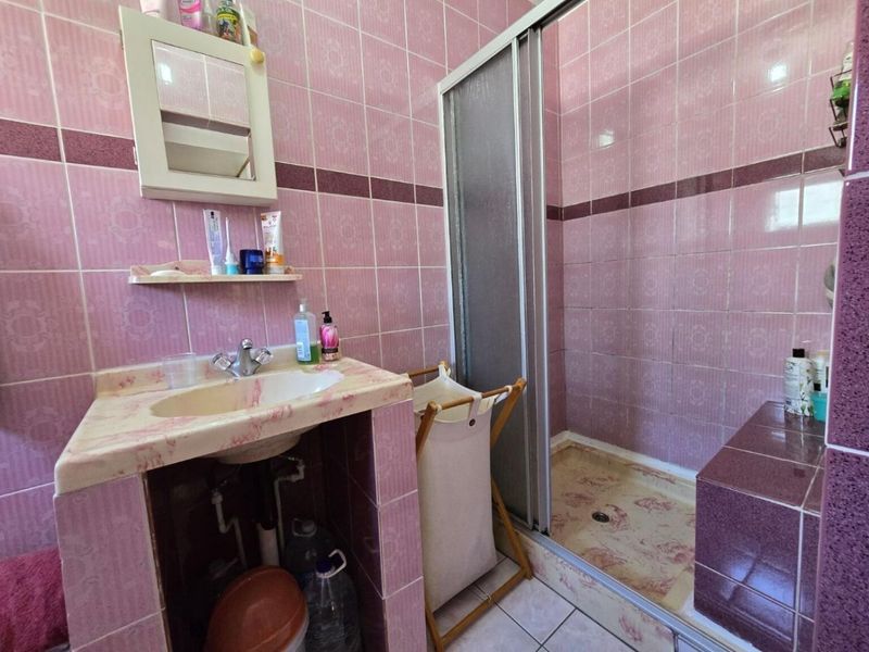 A dated bathroom featuring pink patterned wall tiles, a shower enclosure, and a vanity basin with exposed plumbing.