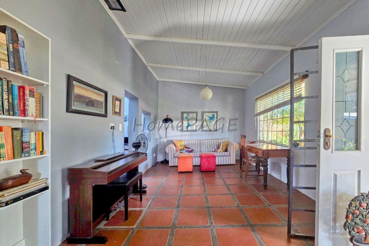 A spacious living room featuring terracotta floor tiles, a white timber-paneled ceiling, and large windows providing natural light.