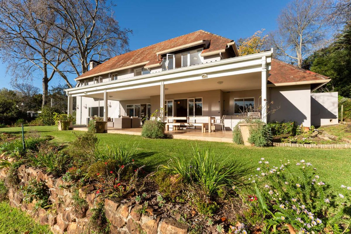 A spacious rear exterior view featuring a large covered patio, tiled roof, and a well-maintained garden with a stone retaining wall.