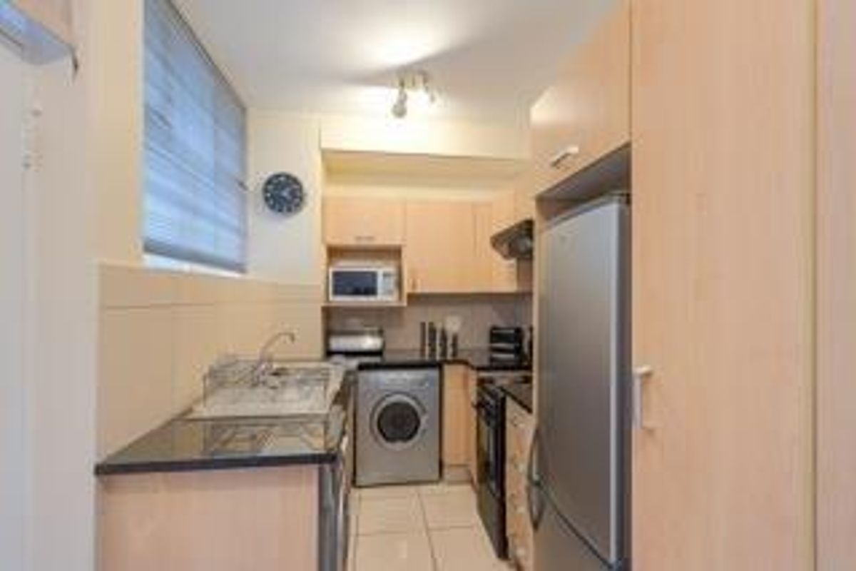 Compact kitchen featuring light wood cabinetry, granite countertops, integrated appliances, and tiled flooring.