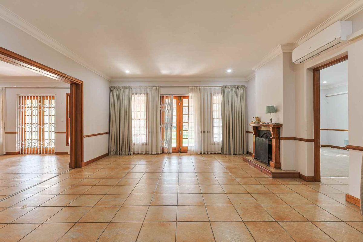 Spacious living room featuring tiled flooring, a traditional fireplace, and split system air conditioning, with direct access to outdoor areas through timber-framed doors.