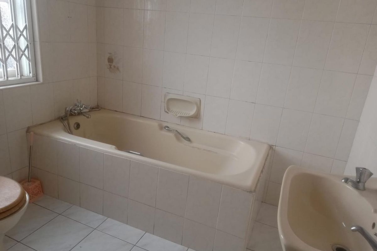 A dated bathroom featuring a built-in bathtub, bidet, and toilet with white wall and floor tiling, requiring cosmetic updates to modernize the space.