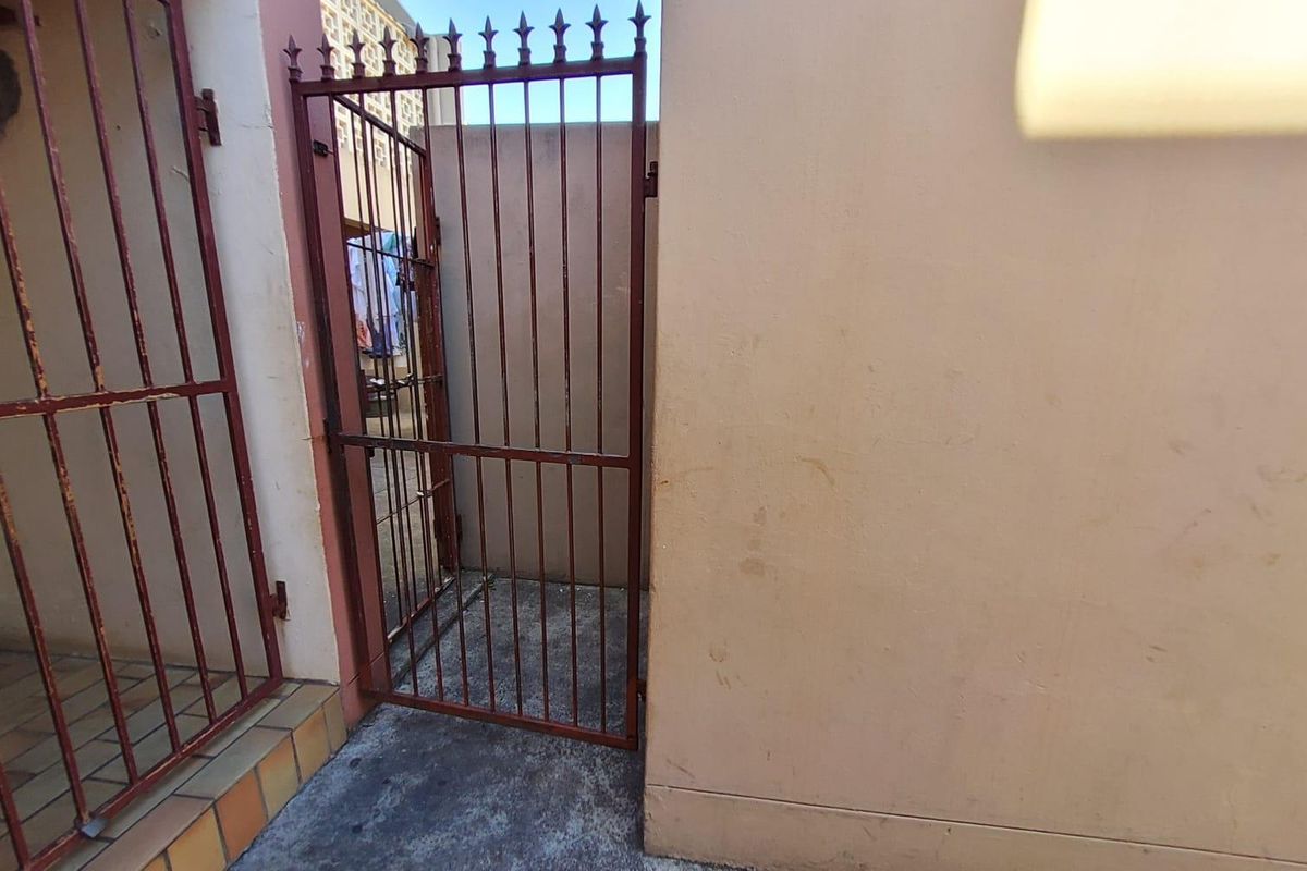 A narrow exterior access area featuring a metal security gate and concrete flooring, providing a functional transition space between property sections.